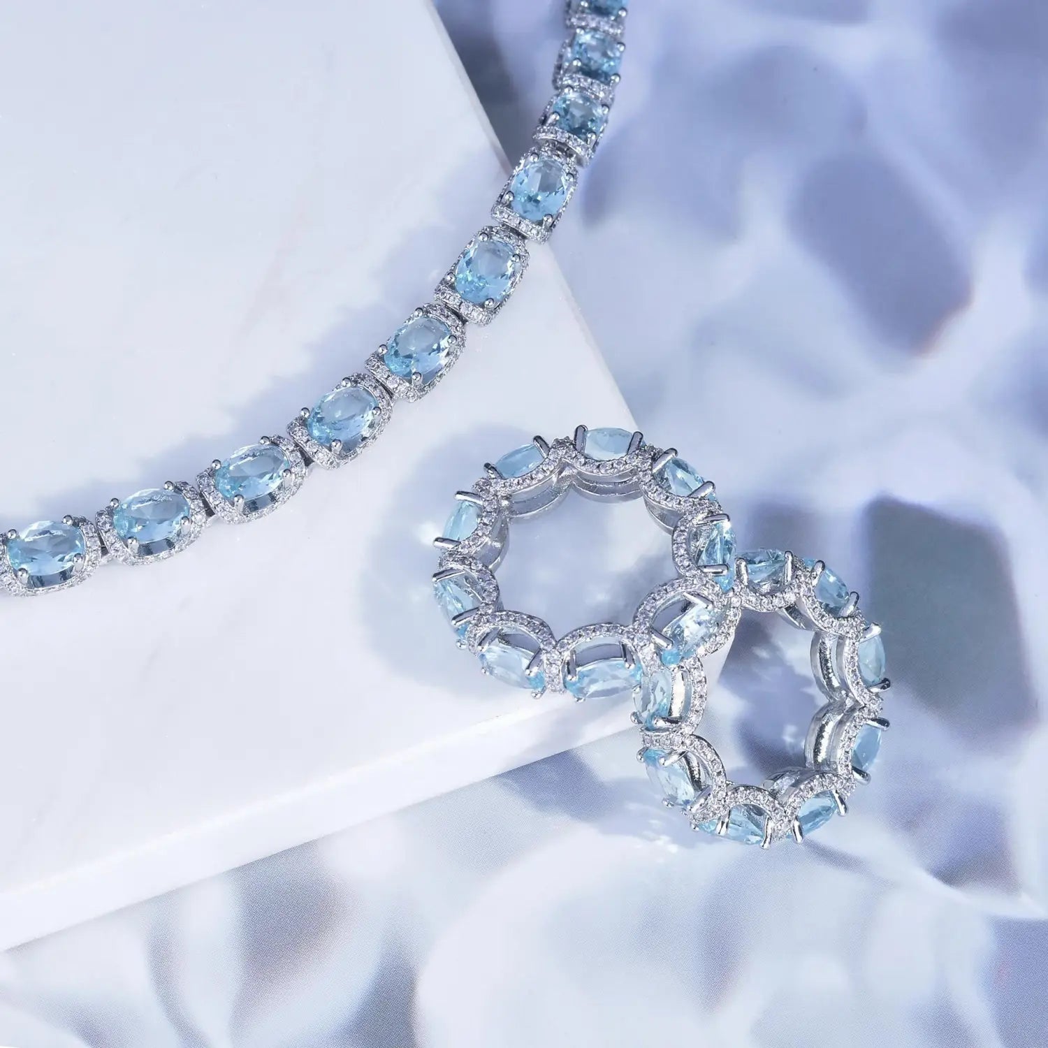 Elegant aquamarine crystal bridal jewelry set featuring a blue topaz necklace and matching ring with oval cut stones surrounded by sparkling diamonds on sleek silver toned metal.