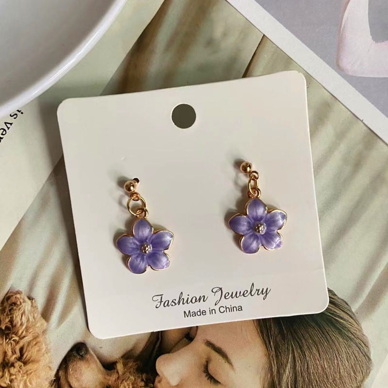 Boucles d’oreilles en forme de fleur émaillée violette, avec des attaches en métal à l’aspect doré, et une petite pierre transparente au centre de chaque pétale ; complètent un collier pendentif de fleur romantique et mignon avec une chaîne à maillons délicate.