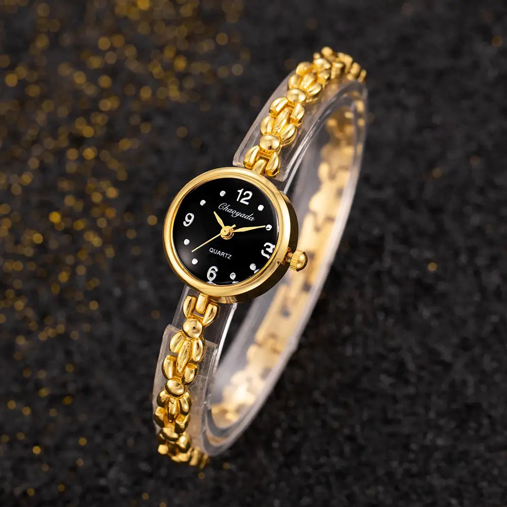 Gold ladies bracelet watch with a small black dial white hour markers and hands featuring a gold-toned chain-link bracelet and quartz movement.