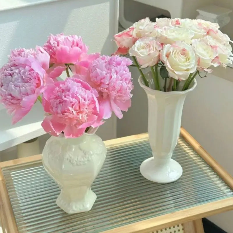 Dos jarrones de cerámica modernos blancos con patrones florales en relieve: uno contiene peonías rosas y el otro, rosas color rubor; ideales para la decoración del hogar con cerámica moderna francesa.