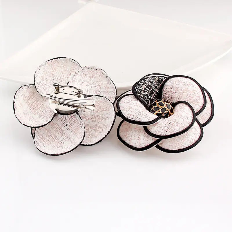 Elegante Brosche aus weißem und schwarzem floralen Kamelienstoff mit strukturierten Blütenblättern und einer goldfarbenen Akzentmitte für Retro-Damenbrosche.