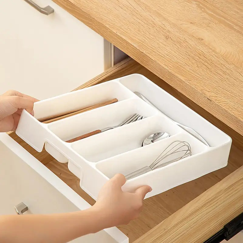 Bac d’organisation réglable pour ustensiles de cuisine en plastique blanc, pour tiroir, avec plusieurs compartiments accueillant des ustensiles et un fouet.