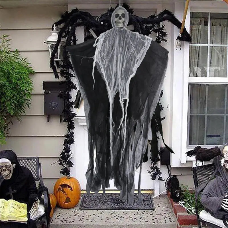 Décoration d’Halloween suspendue en forme de fantôme avec tête de crâne noire et corps en tissu déchiré suspendu à l’avant de la véranda, servant de décoration inquiétante.