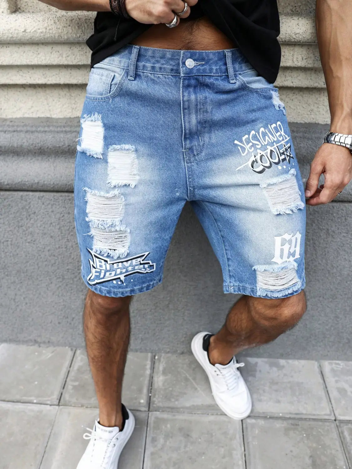 Shorts en jean bleu délavé et déchiré, avec un tissu effiloché et des graphismes de texte style graffiti blanc, pour une tenue d’été.