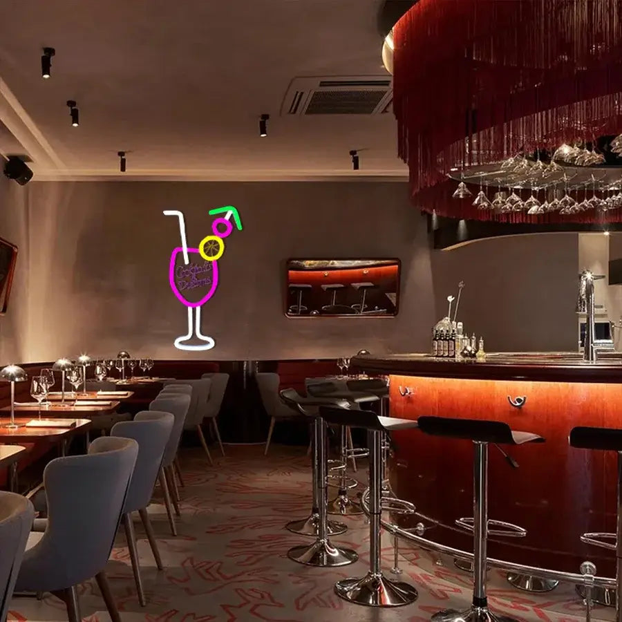 Une enseigne néon vibrante intitulée « Cocktails and Dreams » présentant un verre à cocktail avec des contours pourpres et blancs, ainsi que des accents verts et jaunes pour la paille et la tranche de citron vert.