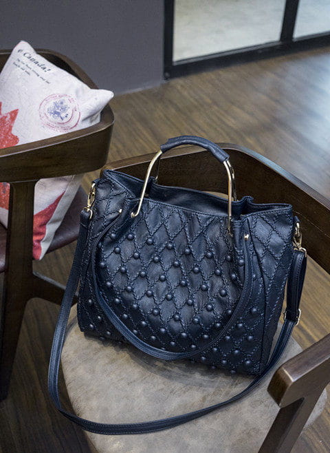 Bolso de hombro de cuero azul oscuro con diseño acolchado, que presenta un asa y una correa para el hombro de tono dorado metálico, y un compartimento interior visible.