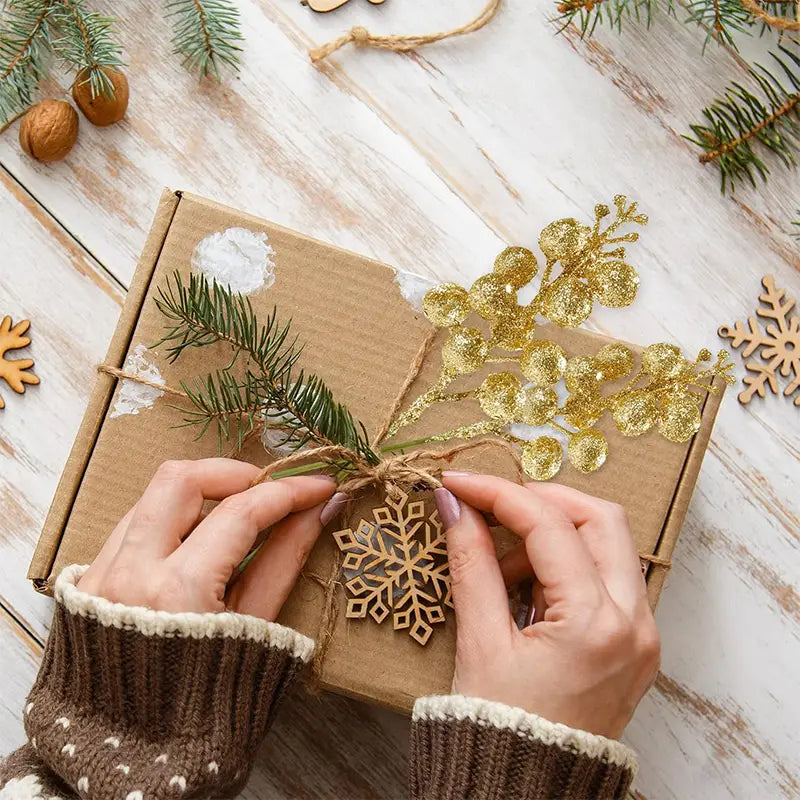 a rustic brown cardboard flower bouquet decorated with natural pine branches gold glittery foliage and a wooden snowflake ornament tied with twine for christmas decoration glitter use
