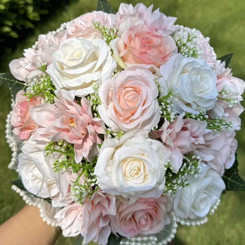 A delicate white silk rose wedding bouquet featuring artificial roses in soft white and blush pink hues with lace, pearls, tiny greenery, and a beaded edge.