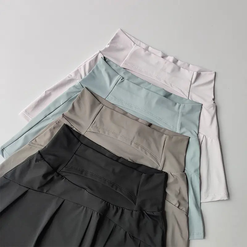 Ein Stapel aus fünf Damen High-Waist-Sport-Tennisröcken in sanften Pastell- und neutralen Tönen, mit plissiertem Design und schnelltrocknendem Material.