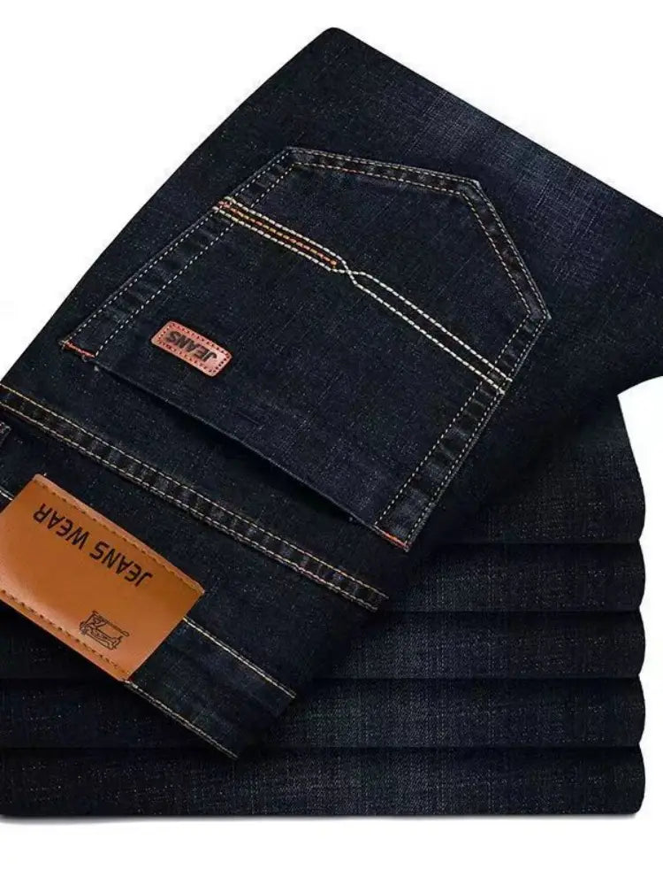 Jeans stretch en denim à jambe droite pour homme en indigo foncé, avec une couture blanche contrastante et des empiècements de marque en cuir brun visibles de l’arrière.