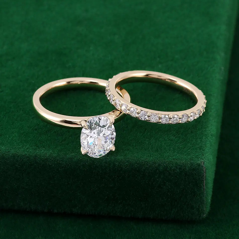 Une paire de bagues, tons or, pour ensemble de bague de fiançailles en diamant de laboratoire ovale : l’une avec une pierre claire facettée en forme ovale et l’autre avec une ligne continue de pierres claires plus petites.
