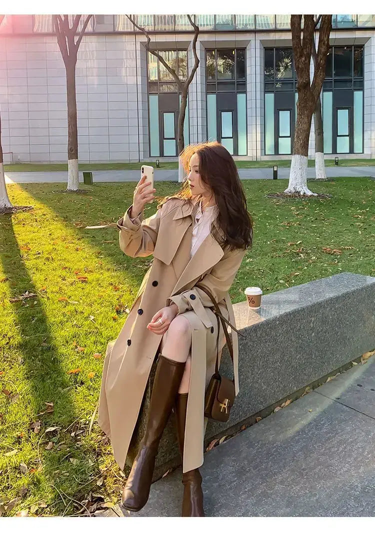 Beige women double-breasted trench coat with black buttons and belted waist designed as a casual windbreaker.