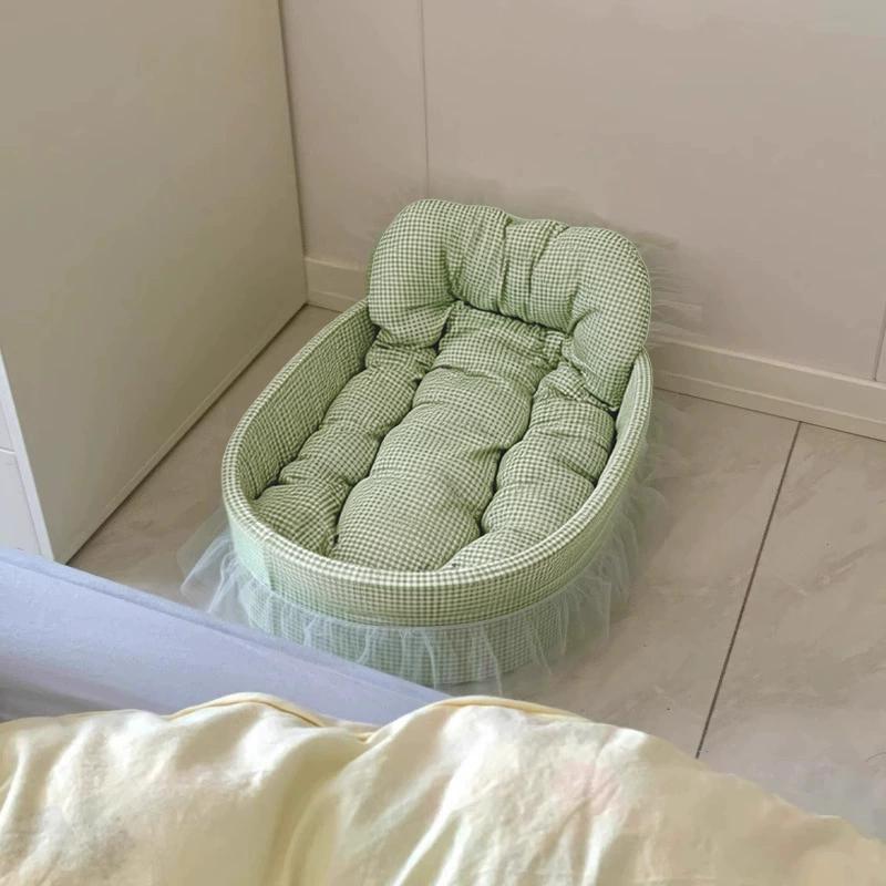 Una cama para mascotas blanda y ovalada de tela, con exterior a cuadros verde y blanco, acolchado acolchado y delicados volantes translúcidos a lo largo de la base, diseñada para perros pequeños.