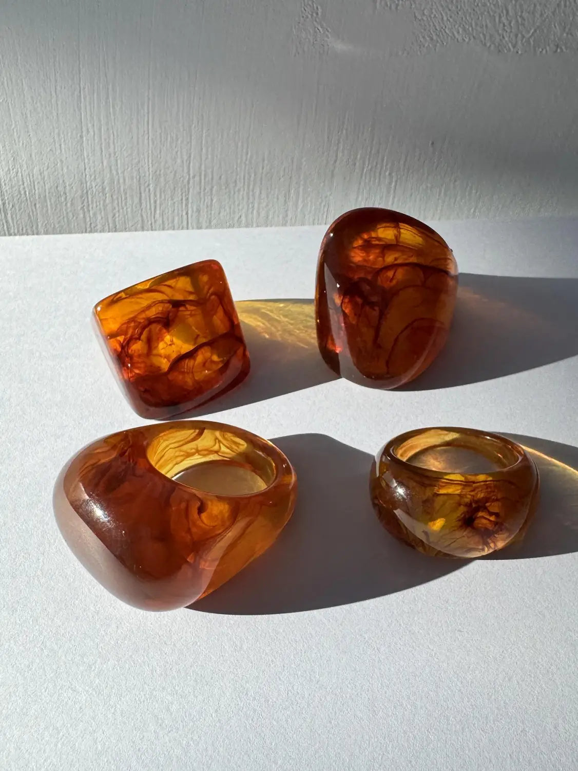 Amber-colored translucent chunky resin cocktail rings set of four with swirling golden and brown patterns.