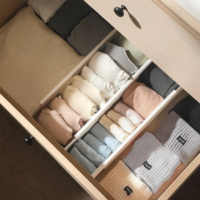 Séparateur extensible en plastique pour organisateur de tiroir, maintenant des chandails en maille douce soigneusement repliés dans des tons neutres beige, crème et gris.