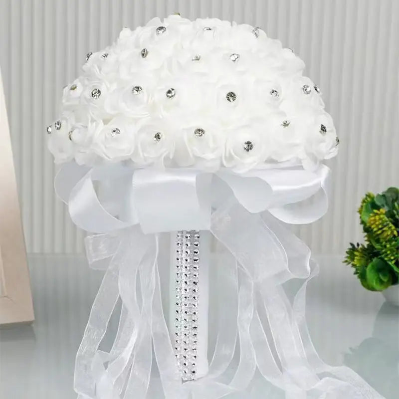 繊細な布製のバラにきらめくラインストーンをあしらった白いラインストーンの結婚指輪リングピローのフローラル・ブライダルブーケで、サテンリボンのボウでアクセントを付けています。