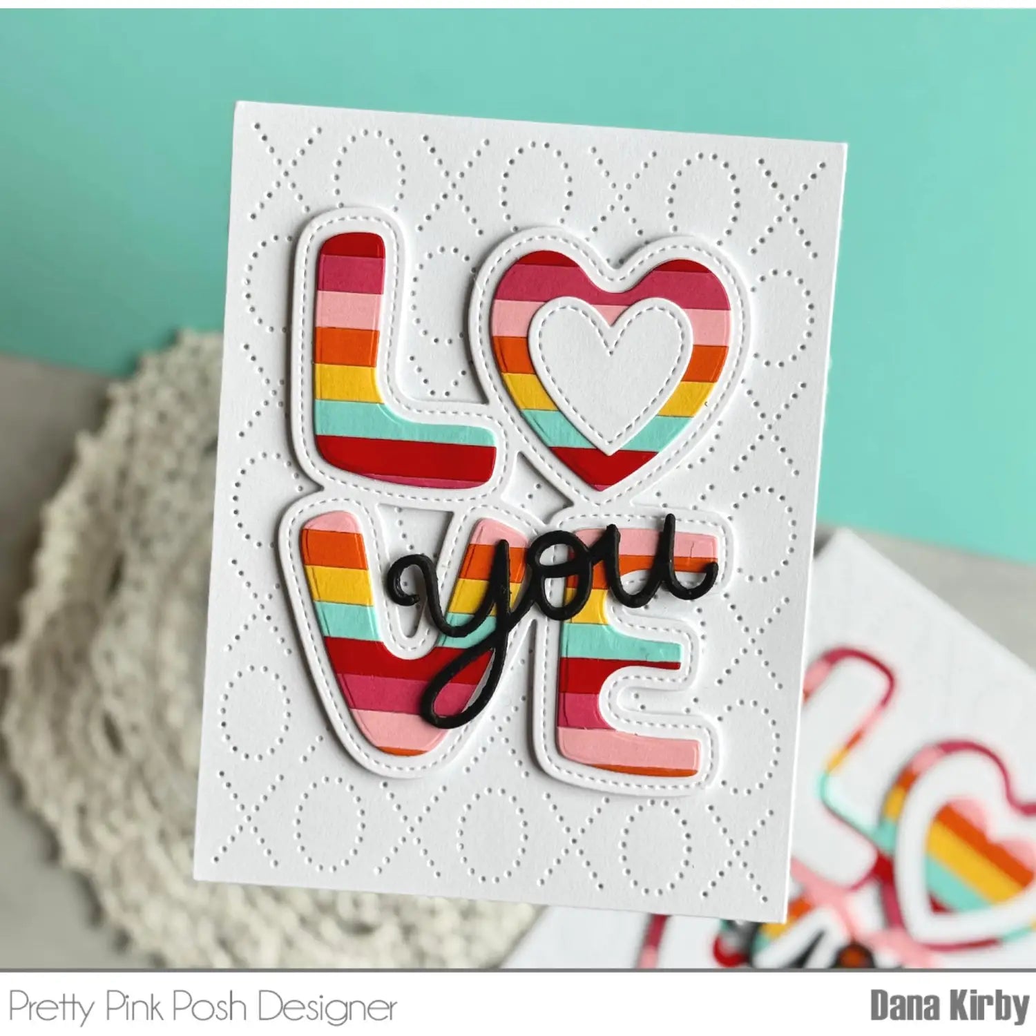Valentine metal cutting dies and clear stamps set featuring a vibrant rainbow-striped love card with a heart-shaped cutout and black cursive script crafted from layered paper.