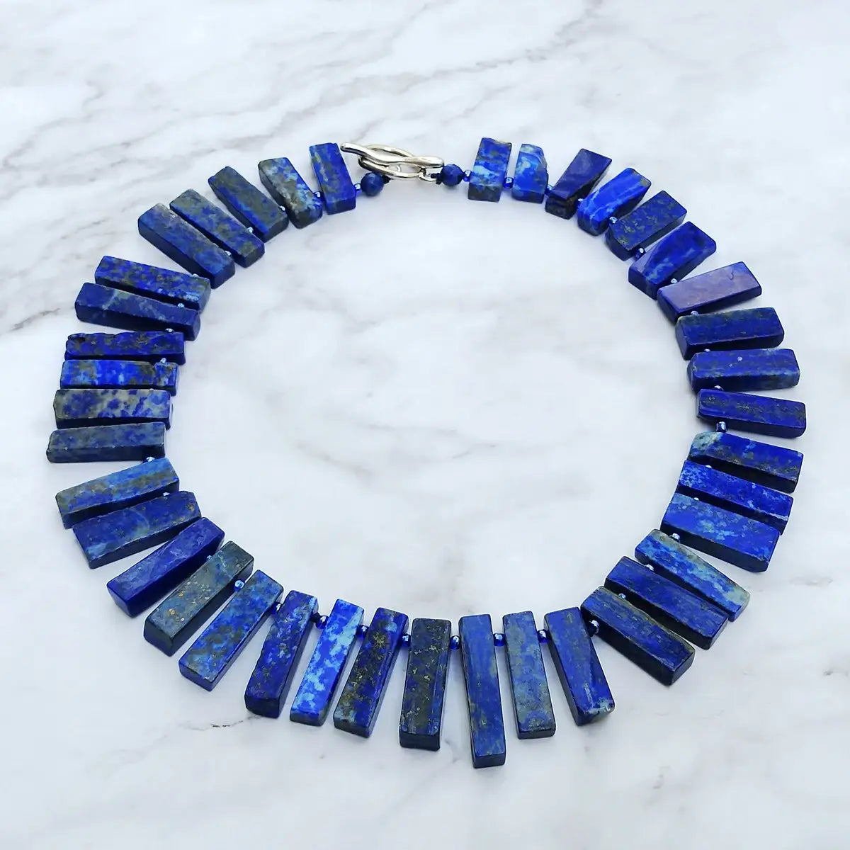 Un collier ras du cou audacieux en lapis-lazuli bleu profond, présentant des perles de pierre polie rectangulaires à veines naturelles et une fermeture à bascule à tons argentés, bijouterie de déclaration en pierre précieuse.