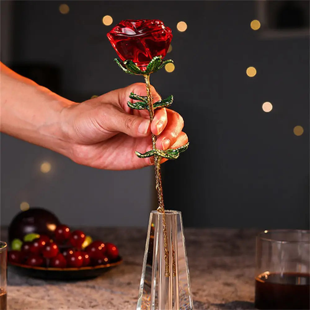 A translucent red crystal glass rose with green beaded leaves and stem held above a clear crystal vase, designed as a Valentine’s Day gift.
