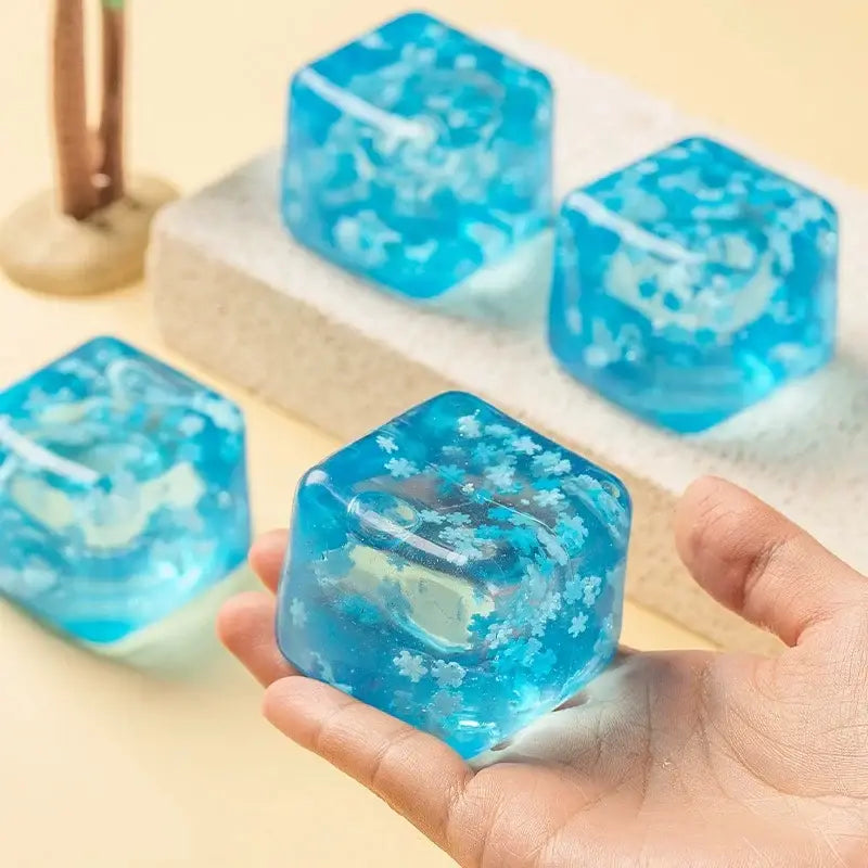 vue de face d’un cube sphérique translucide bleu à faible rebond, visqueux et lent, façonné comme un glaçon, avec des motifs floraux blancs intégrés