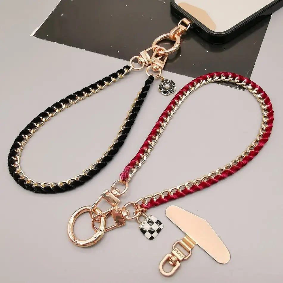 zwei geflochtene Handy-Handgelenkriemen-Goldketten in Schwarz und Gold mit einem silberfarbenen floralen Anhänger sowie in Rot und Gold mit einem karierten Schloss-Anhänger für Anti-Lost-Handylanyard-Verwendung