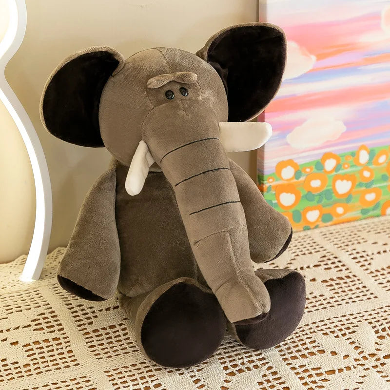 Un peluche de animal de la jungla que presenta un elefante gris claro suave con orejas internas negras y patas blancas, colmillos de textura detallada y costuras elaboradas.