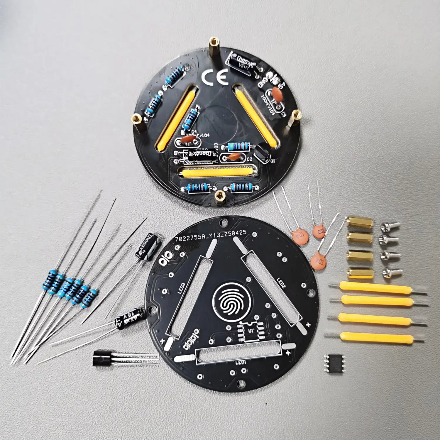 placas de circuito circular negras con tiras de LED amarillas y componentes electrónicos dispuestos alrededor de ellas en un kit de soldadura DIY de LED regulables mediante contacto.