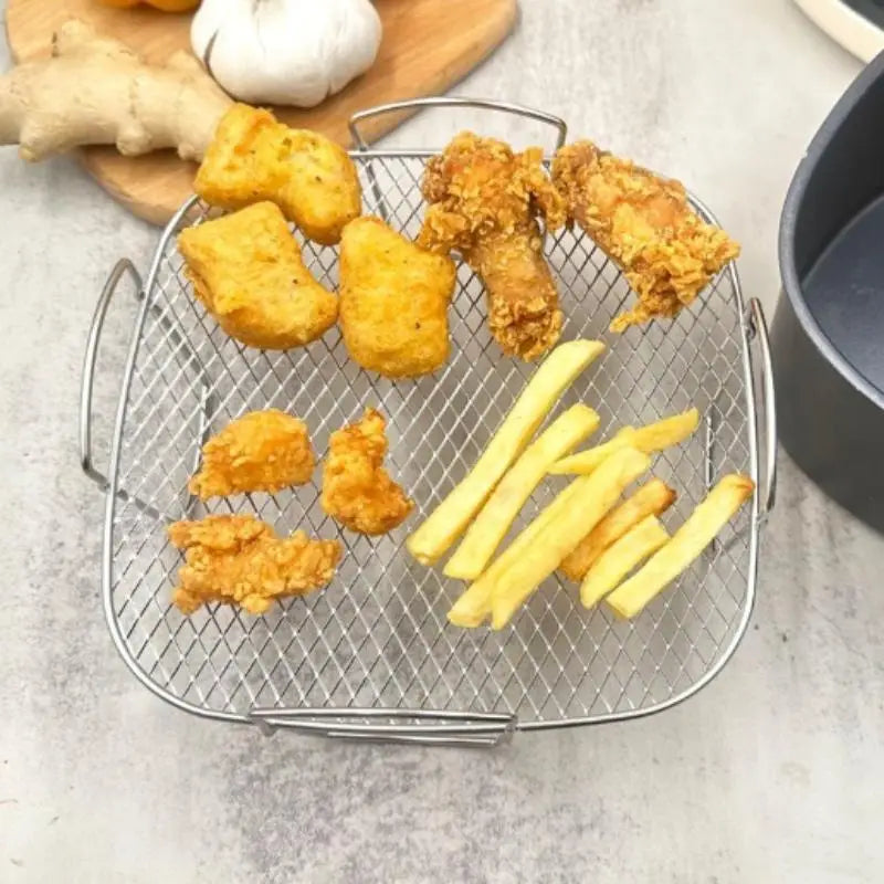 Edelstahl-Luftfritteusen-Grillrost als stapelbarer Korb in Silber mit Drahtmaschen, mit Griffen, die goldbraune Stücke von gebratenem Hähnchen und Pommes frites enthalten.