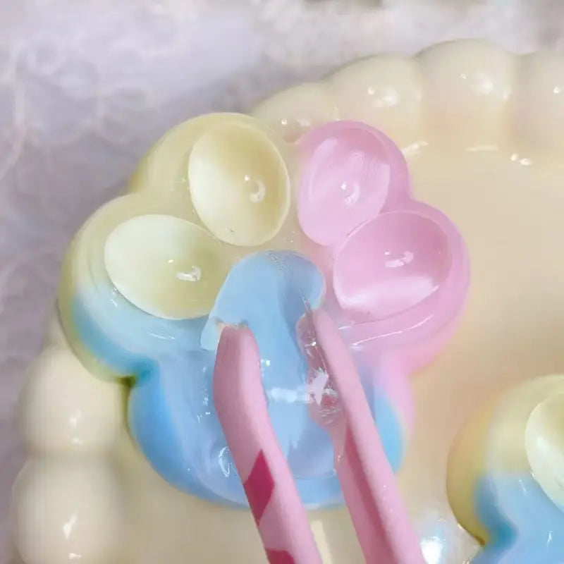 Le jouet anti-stress souple et moelleux en forme de griffe de chat arc-en-ciel est un objet souple et moelleux translucide, à empreinte de patte, de couleur pastel, inspiré d’un dessert, avec des nuances douces de jaune, rose et bleu.
