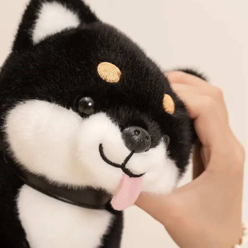 A plush shiba inu dog stuffed animal toy featuring black and white fur with tan embroidered markings, glossy black eyes, and a pink tongue sticking out.