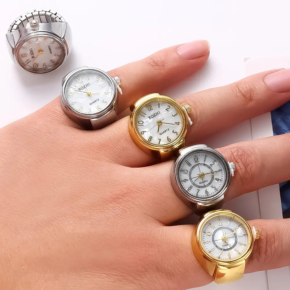 A hand adorned with five miniature ring watches featuring gold and silver metallic casings, white faces with black numerals, and the brand bozhi printed on each dial, part of the ring watch quartz finger jewelry unisex gift collection.