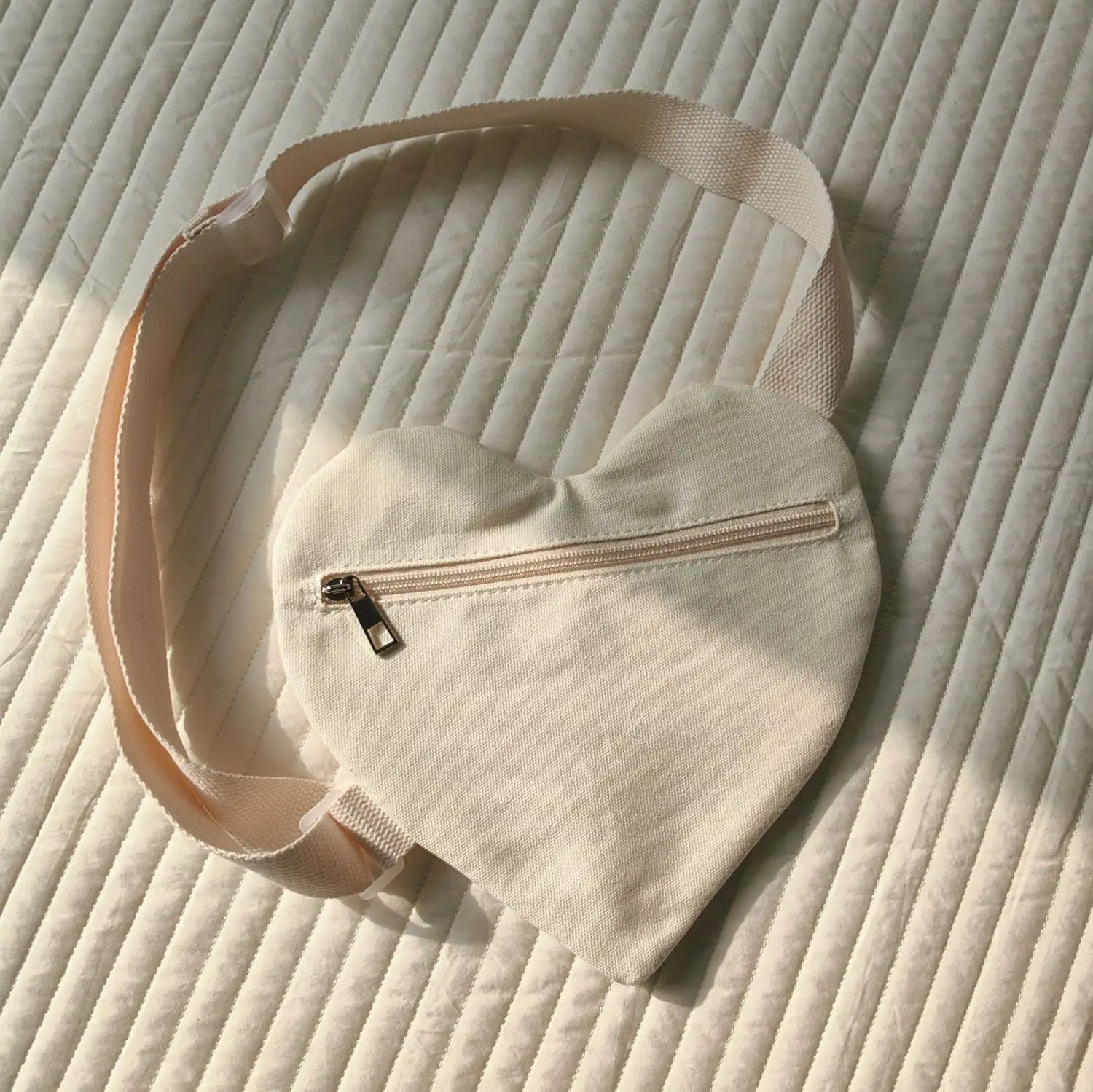Eine weiche cremefarbene herzförmige Canvas-Umhängetasche mit passendem verstellbarem Träger und Front-Reißverschluss, ausgelegt für koreanische Kinder.