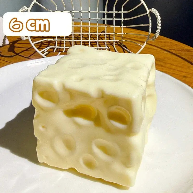 A creamy off-white cube-shaped cheese squishy toy with a realistic swiss cheese pattern of holes shown from the front for stress relief.