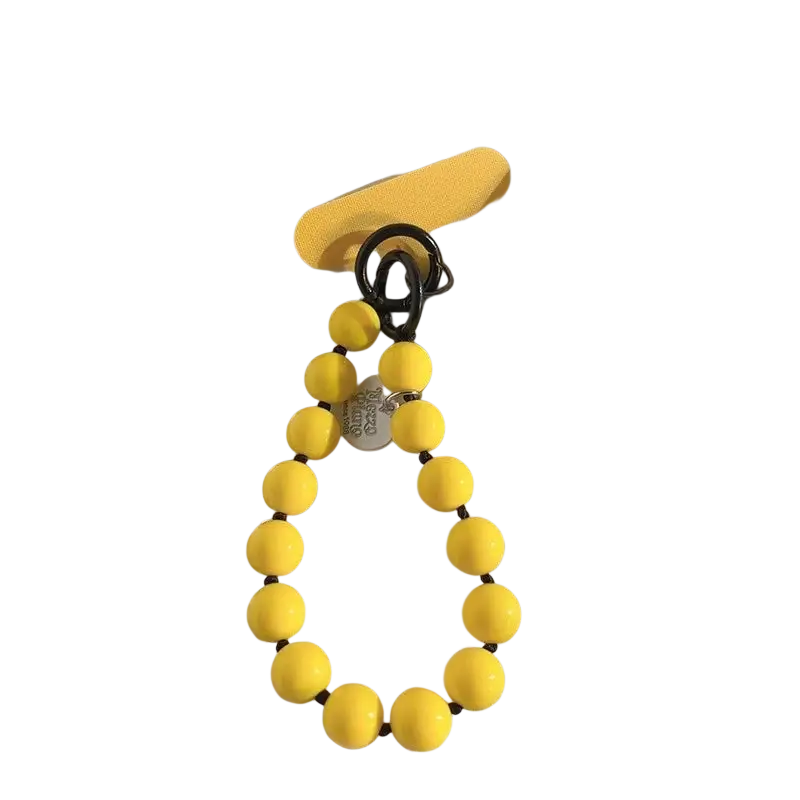 Correa de muñeca para teléfono con cuentas amarillas y dijes con forma de corazón, con un broche de metal negro y un lazo de silicona amarillo a juego mostrados desde un ángulo de cerca.
