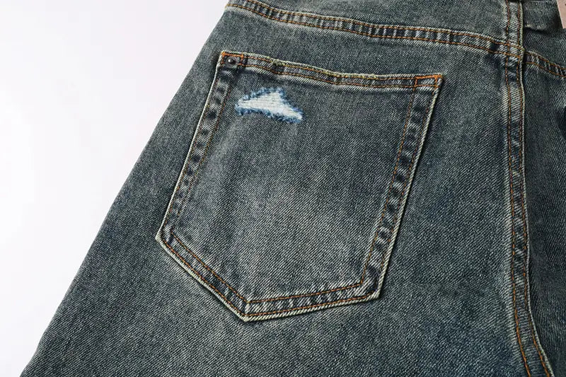 The back side of men’s distressed blue acid wash denim shorts featuring dark-wash denim with a distressed patch on the back pocket and visible faded blue thread stitching.
