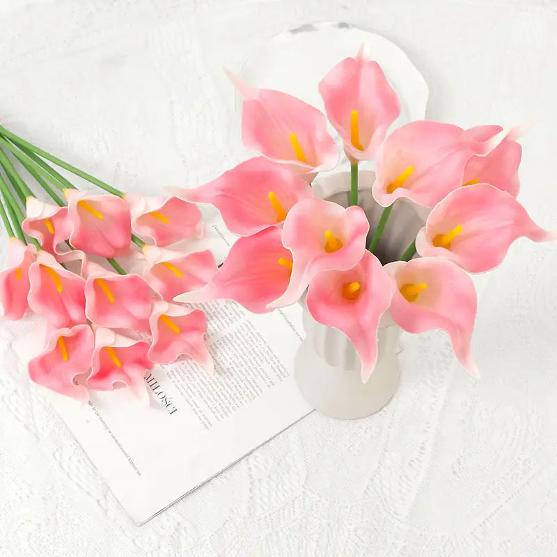 A front view of a flower bouquet featuring pink calla lily blooms with yellow centers arranged in a white ceramic vase for home decor.