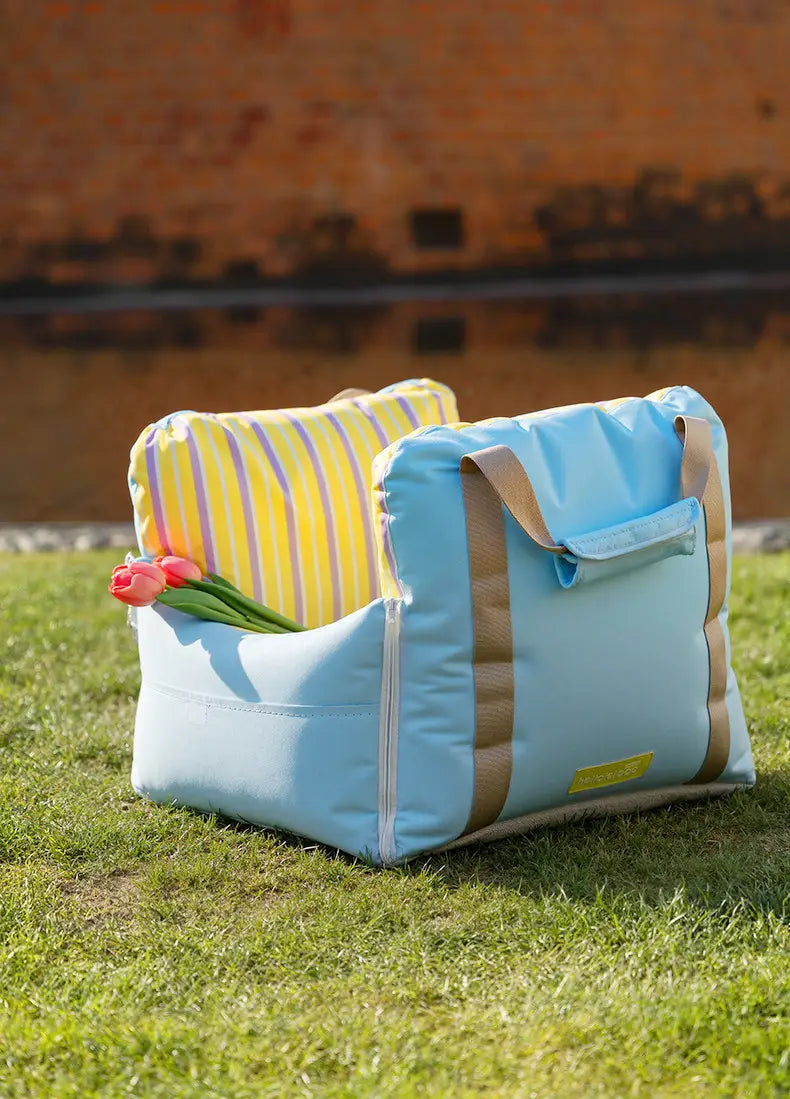 Siège de voiture pour chien et lit de voyage souple bleu clair, avec poches frontales et sangles en toile camel, ainsi qu’un coussin à rayures jaunes à l’intérieur.