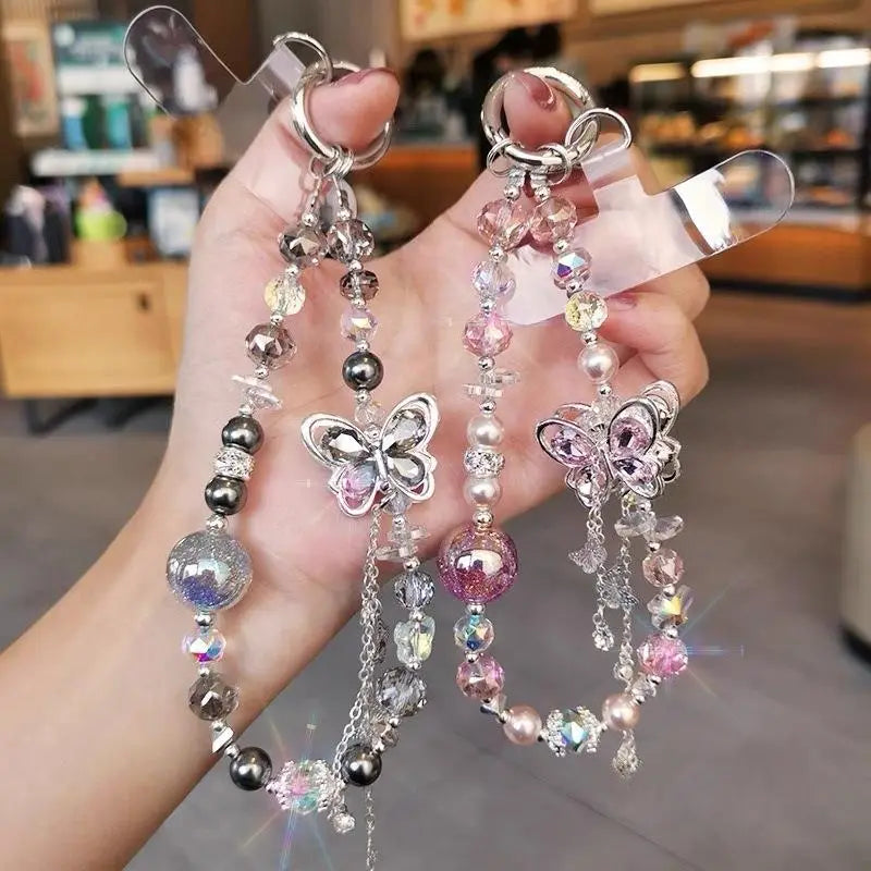 Deux porte-clés décoratifs de chaîne pour téléphone arborant des breloques papillon argentées avec des cristaux roses scintillants et transparents, ainsi que des perles irisées aux teintes noires, grises et roses scintillantes pour un usage avec le téléphone mobile.