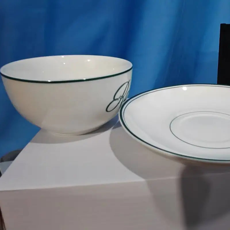 White ceramic coffee cup and saucer set with a vintage green rim and an elegant black scripted monogram on the side.