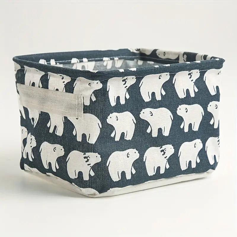 Panier de rangement pliable en tissu bleu marine avec des motifs d’ours polaires blancs et une lanière de poignée en plastique transparent, conçue comme une boîte de rangement polyvalente.