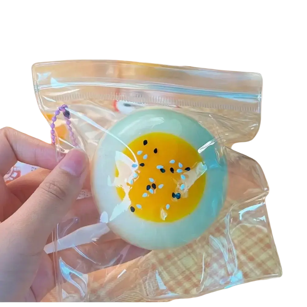 A front view of a translucent soft squishy toy shaped like a pale blue egg yolk pastry with yellow yolk and black sesame seeds
