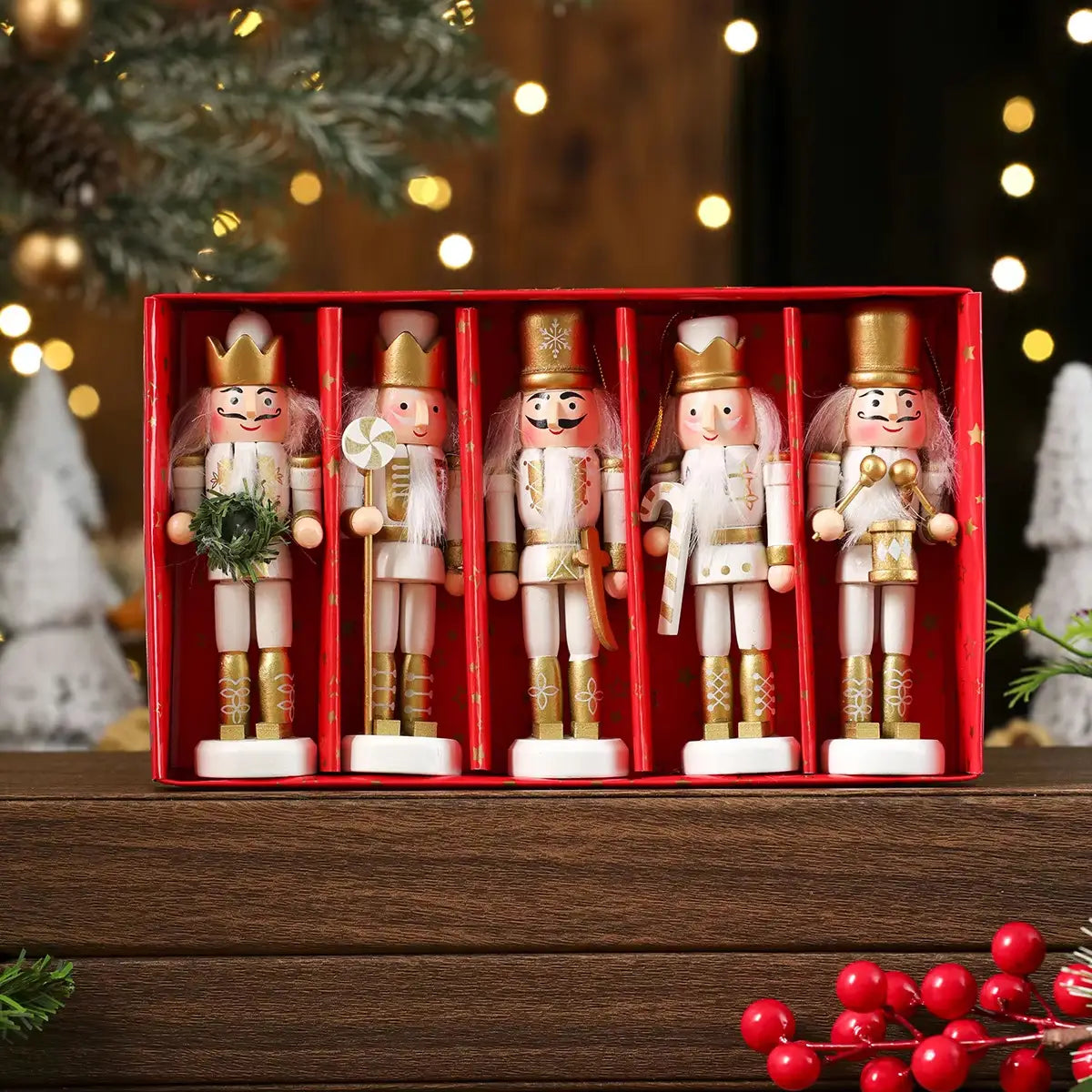 Cinco figurines de adorno para árbol de Navidad de cascanueces de madera con detalles blancos y dorados, dispuestos en una caja roja, vistos desde arriba.