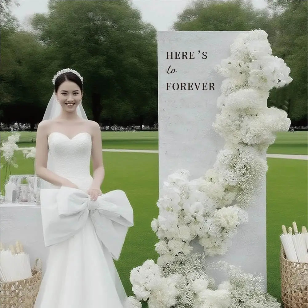 robe de mariée en satin blanc, avec un grand nœud à la taille, présentée aux côtés d’un panneau de bienvenue de mariage personnalisé en tissu.