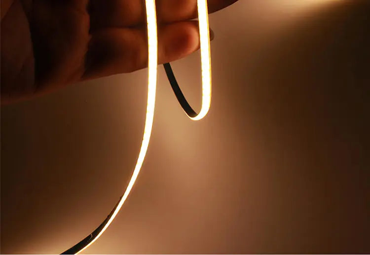 Una tira flexible de LED COB de luz blanca cálida con respaldo negro elegante, mostrada desde una vista frontal en ángulo, para decoración del hogar de bricolaje