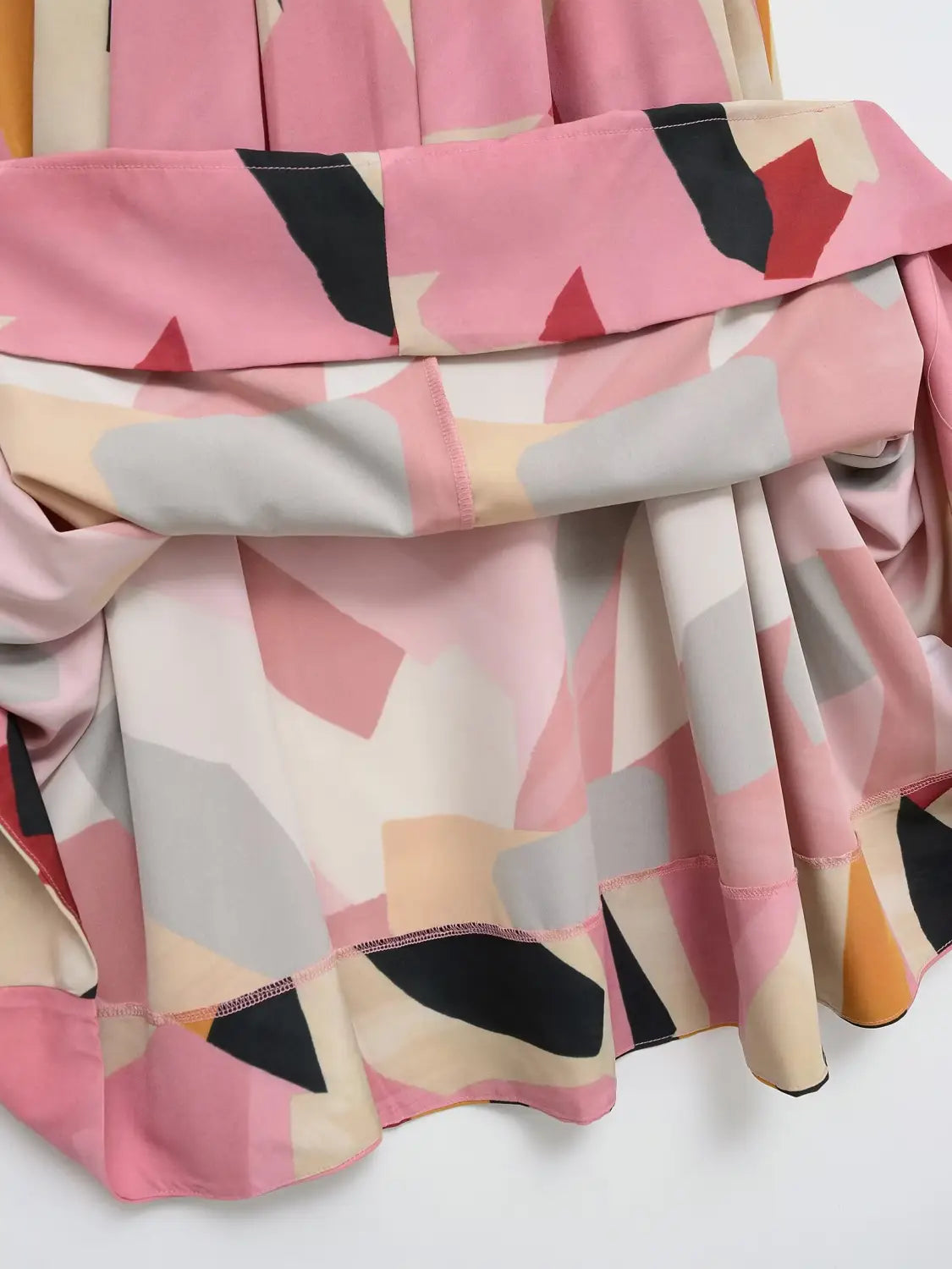 Ein geometrischer Satin-Midirock mit fließendem Design und einem modernen geometrischen Muster in Schattierungen von Rosa, Beige, Schwarz und Orange.