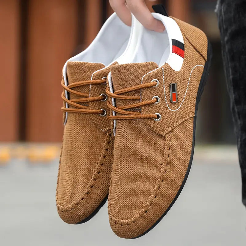 Men’s casual canvas sneakers in brown with tan laces and white interior lining featuring a small red and black stripe detail on the collar designed as lightweight daily footwear.