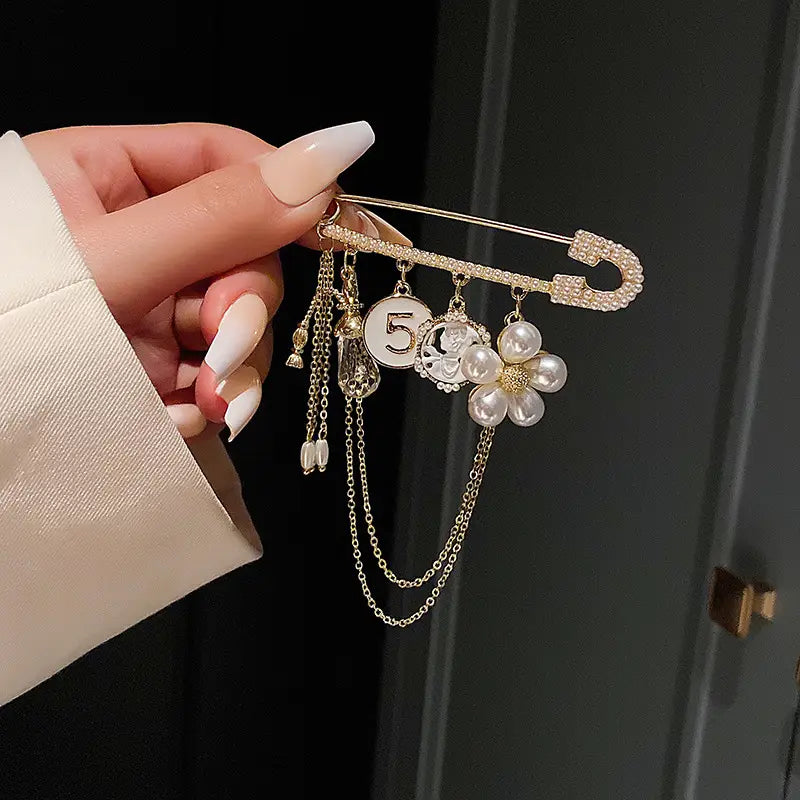Gold-toned safety pin brooch pearl flower number 5 adorned with sparkling rhinestones and dangling pearl flower and circular charm pendants suspended by delicate chains.