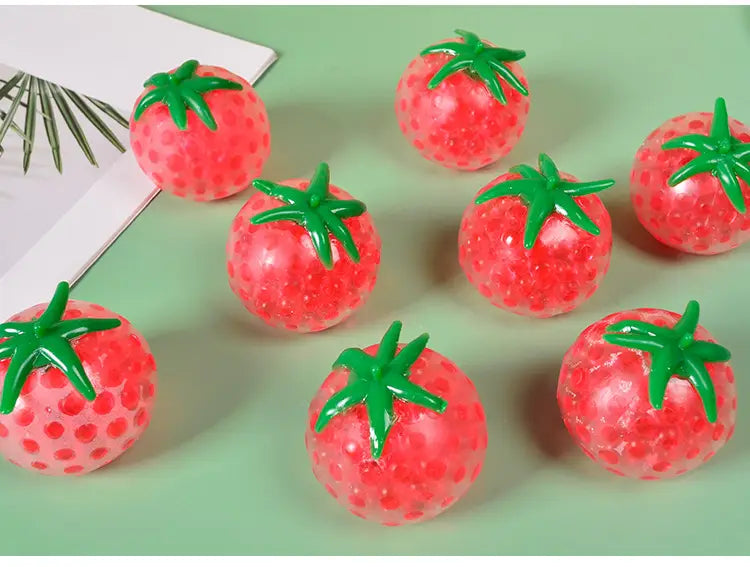 Red tomato-shaped squishy stress relief toy made of gel bead-filled material with a textured surface and green plastic stems for squeezing.