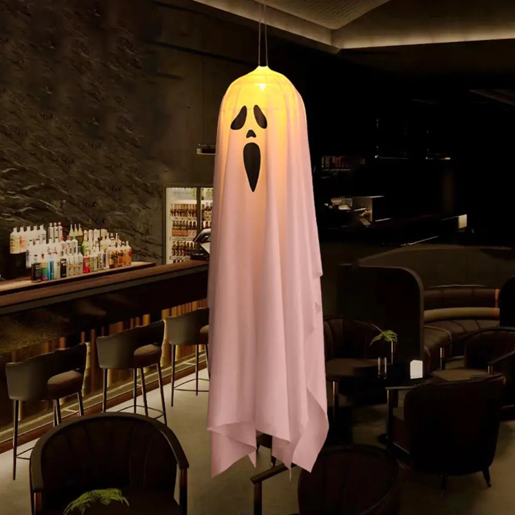 a glowing pink led hanging ghost halloween decoration pendant light with a black face design hangs from the ceiling