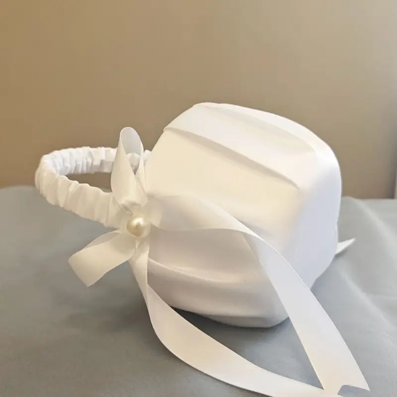White satin wedding flower basket with a gathered elastic band and a pearl-adorned bow used in a bridal bouquet and ring pillow set.